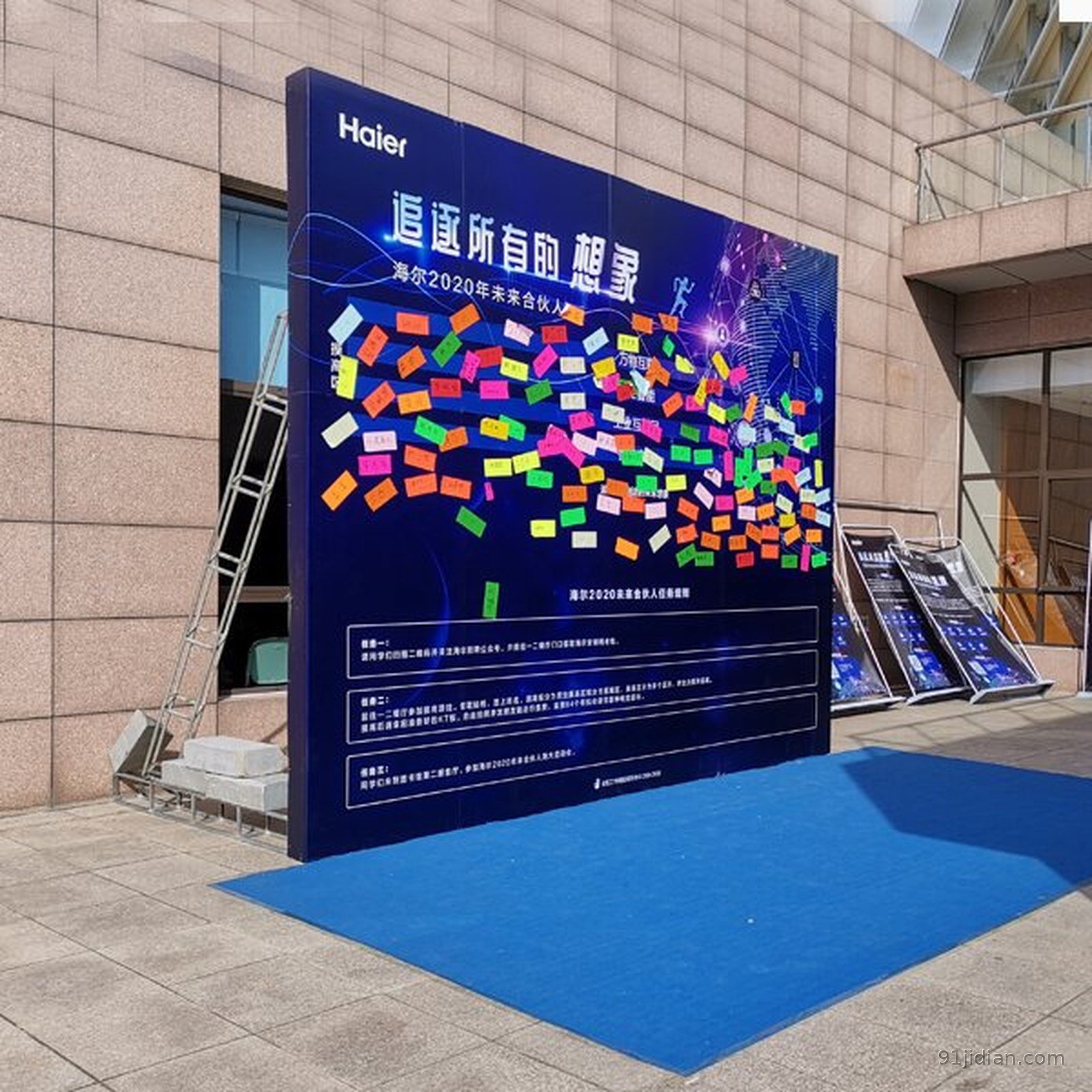 青岛年会背景板搭建现场：整面活动背景板立于场地，画面印有活动主题与品牌元素，属临时事件背景而非固定形象墙