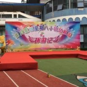 青岛会议背景板实拍：活动现场整面喷绘背景墙配红地毯舞台，属临时搭建年会背景而非前台永久LOGO金属墙