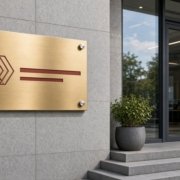 青岛公司铜牌制作示意:办公楼门口花岗岩外墙上用四颗不锈钢广告钉固定的钛金公司牌,表面拉丝金色,蚀刻红色LOGO与字条